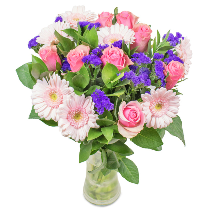 Set against a crisp background, this vivid yet refined bouquet makes a statement for New Eltham residents who value both freshness and classic style. At its heart are seven to nine pink roses, some still tightly closed, others gracefully opening to display their intricate spirals-each blossom a tribute to timeless romance. Interspersed are five to seven pale pink gerbera daisies, their large, round heads and radiating petals evoking the effortless beauty of early spring. Touches of bright purple statice, reminiscent of the wildflowers found near Avery Hill Park, weave between the blooms, adding dimension and a burst of depth. Lush dark green foliage forms a welcoming base, enhancing vibrancy and giving the sense that the bouquet was gathered in a flourishing garden. The stems are laid neatly in a clear glass vase, immersed in water, highlighting the arrangement's artful construction and natural freshness. Perfect for marking a birthday, a special milestone, or simply adding a cheerful note to an everyday space, this floral arrangement from Florist New Eltham is designed to communicate joy, celebration, and sincere affection-blossoming with the character and warmth of SE9.